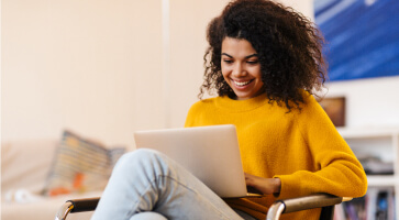 Woman in yellow using laptop while smiling