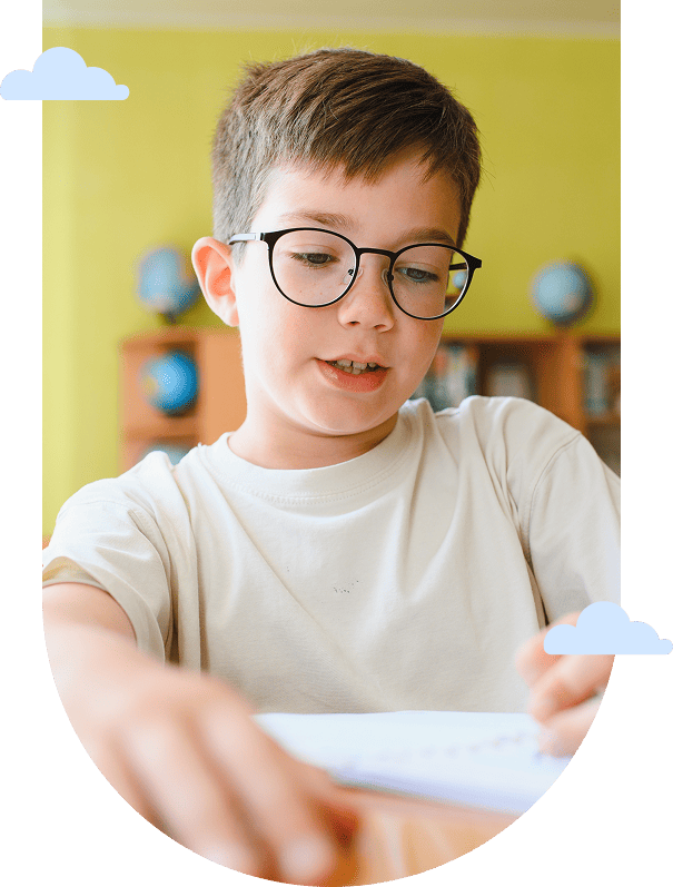 young boy with glasses writing at a desk in a classroom
